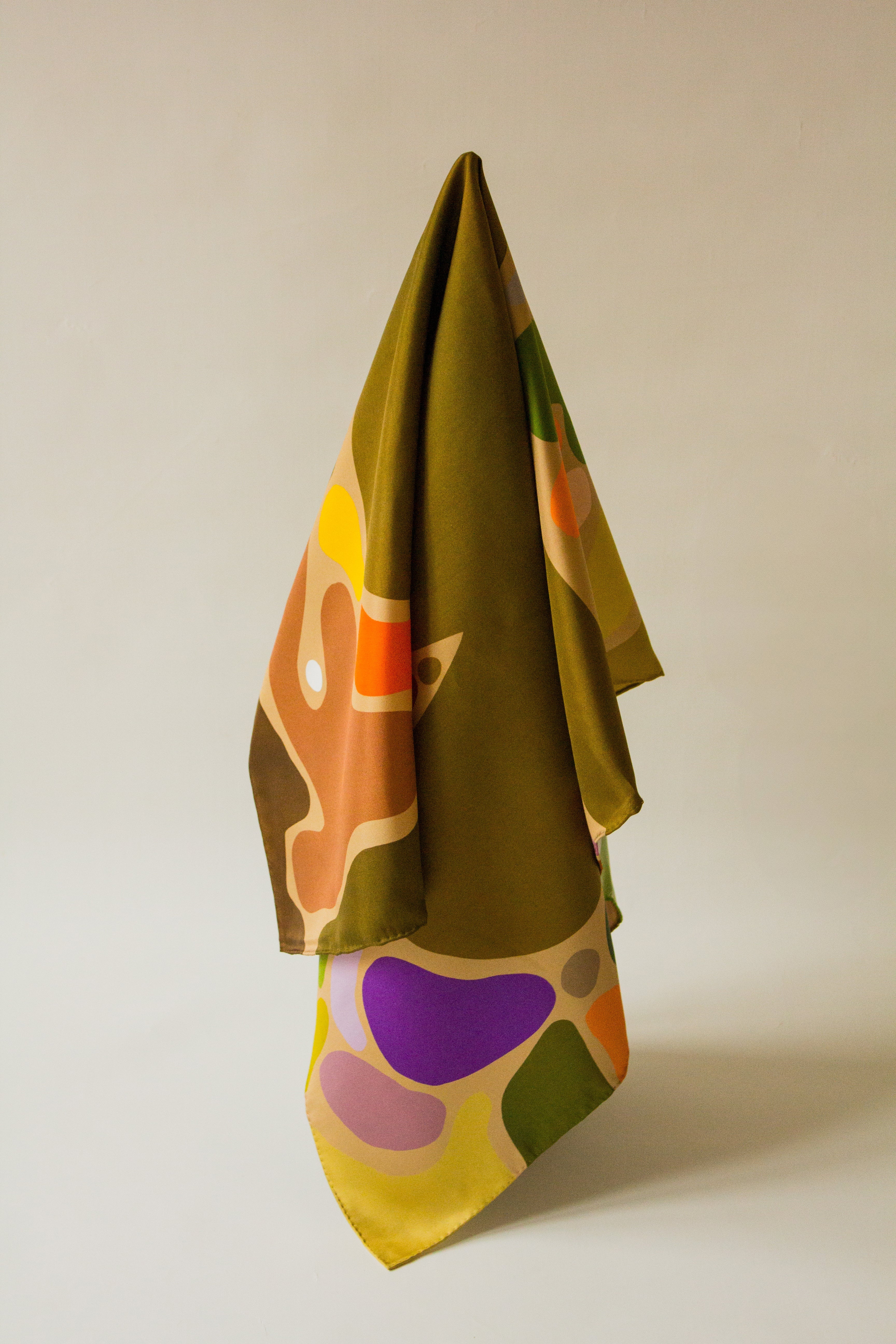 Eat Your Greens Silk Scarf by Kunst & Colore, featuring organic forms coloured in natural tones and bright pops of colour on an oaty beige background.  The scarf hangs artistically on a white background.
